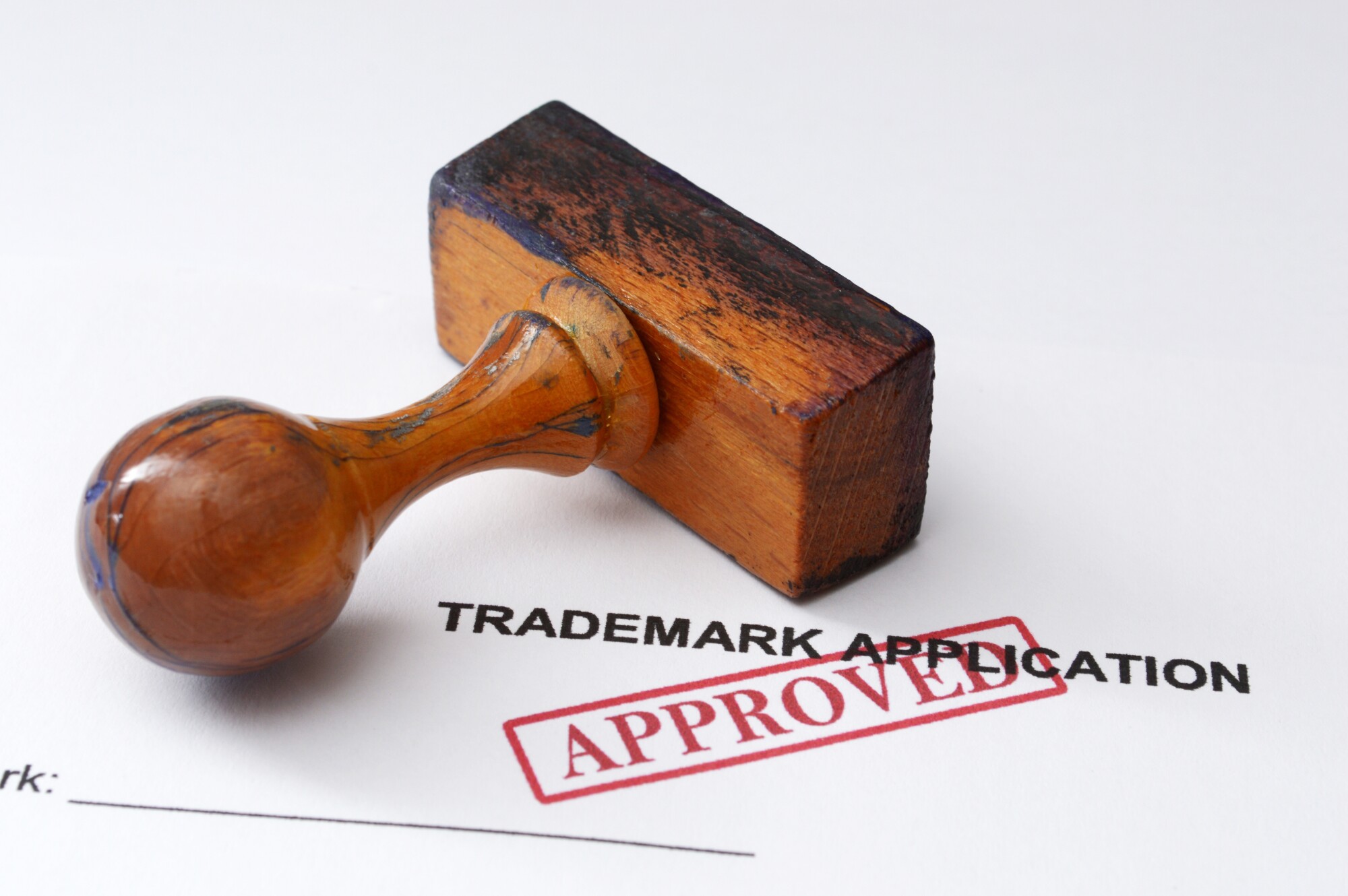 Wood ink stamp laying sideways with red stamp approved over trademark application