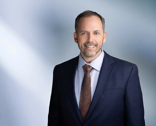 Man, Mikhail Murshak, with short dark hair wearing a navy blue blazer, smiling slightly against a blurred white and blue background.