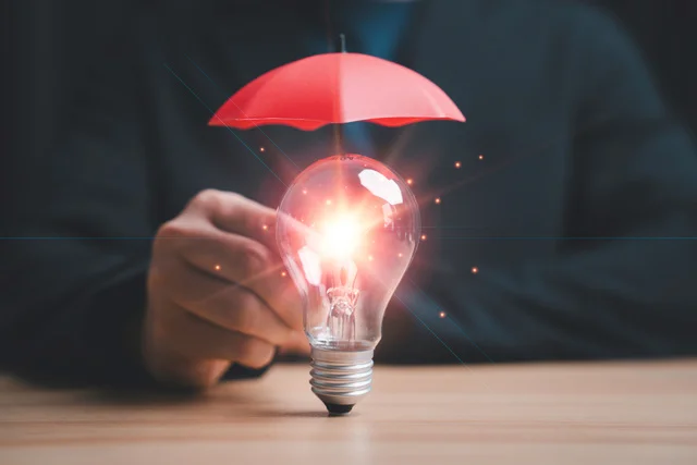 Copyright and patent protection concept with glowing light bulb under red umbrella, intellectual property security, legal rights protection, innovation safeguard and business risk management strategy.
