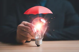 Copyright and patent protection concept with glowing light bulb under red umbrella, intellectual property security, legal rights protection, innovation safeguard and business risk management strategy.